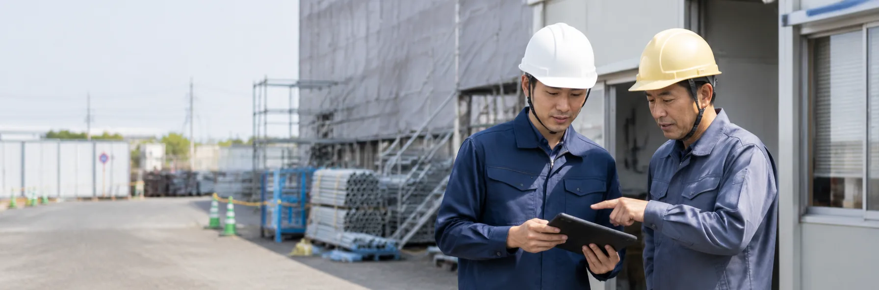 建設現場でタブレットを見ながら打ち合わせをしているヘルメット姿の作業員2名